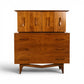 Young Manufacturing sculptural walnut highboy dresser front view with carved bowtie cutout doors and oval drawer pulls