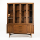 Broyhill Sculptra MCM walnut two-piece china cabinet, full front view showing four-door glass hutch displaying glassware on interior shelves, buffet base with three drawers and carved panel doors, c. 1960s